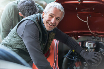 Portrait smiling mechanic fixing engine in auto repair shop - obrazy, fototapety, plakaty