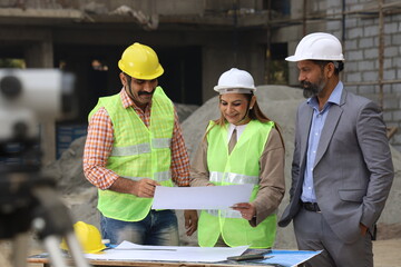 Indian construction workers. Construction engineers working on a builder construction site. Wearing white and yellow helmet analyzing blueprint of property. Reporting, maintaining the work in progress