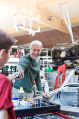 Smiling father taking tool from son in auto repair shop
