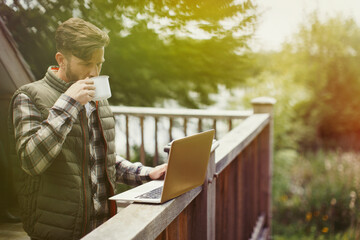 Man drinking coffee and using laptop on cabin deck