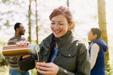 Smiling woman pouring coffee from insulated drink container in woods