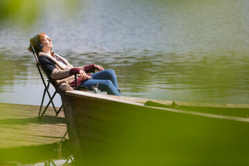 Serene woman relaxing listening to music headphones at sunny lakeside dock