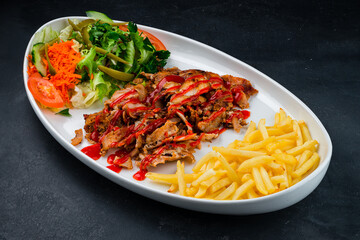 Fried meat with french fries and a salad of pickled cucumbers, tomatoes, carrots, lettuce, parsley and ketchup, shawarma without lavash in a plate.