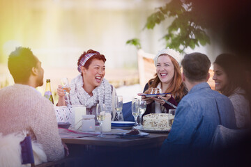 Friends laughing eating cake and drinking champagne at patio table
