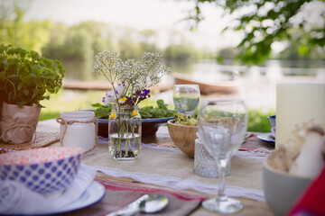 Place settings and simple bouquet on garden party table at lakeside
