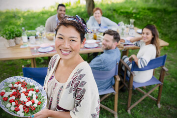 Portrait smiling woman serving Caprese salad to friends at garden party table