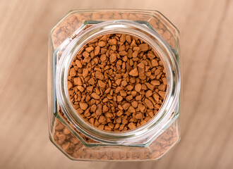 Top view of an open glass jar with instant coffee granules on a wooden background.