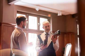 Businessman being fitted for suit examining dress shoes in menswear shop