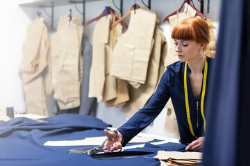 Female tailor cutting fabric in menswear workshop