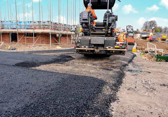 Asphalt paver filled with hot tarmac laying new road surface on new residential housing development...