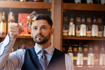 Serious well-dressed bartender examining whiskey