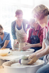 Teacher guiding mature students at pottery wheels in studio