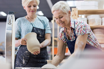 Senior woman holding pottery at kiln in studio - obrazy, fototapety, plakaty