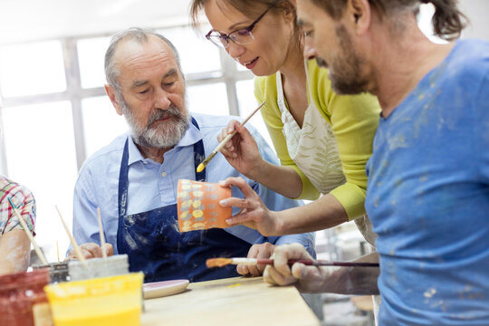 Teacher and mature students painting pottery in studio