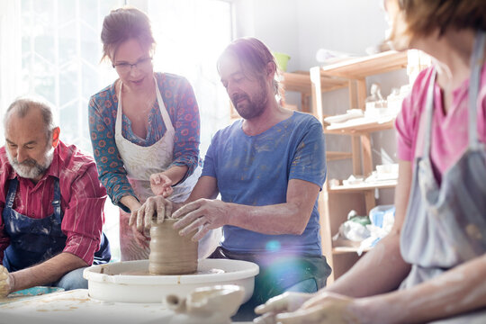 Teacher guiding mature man at pottery wheel in studio