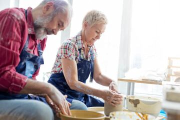 Senior couple using pottery wheels in studio - obrazy, fototapety, plakaty