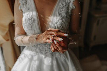 the bride in a white dress puts a gold wedding ring on her finger. French manicure. Open shoulders....