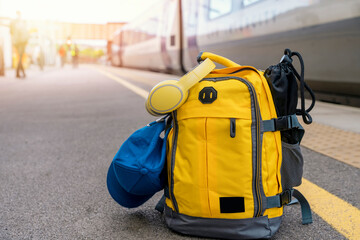 Yellow backpack with headphones and cap on the platform in a train station. Travel touristic concept. travel light