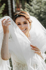 Portrait of beautiful bride in white wedding dress with modern hairstyle and veil walking on garden, front view. Wedding concept