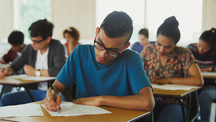 Male college student taking test at desk in classroom