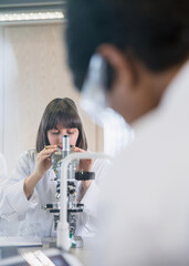 Female college student using microscope conducting scientific experiment in science laboratory...