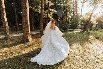 Beautiful bride in a wedding dress with a long train standing back in the forest.