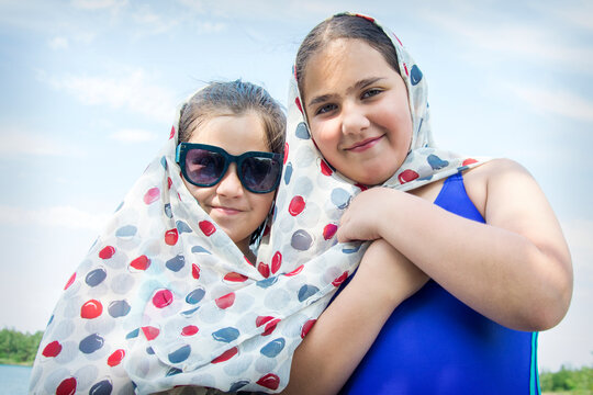Two girls with a big scarf on the beach. The girls hold a developing pareo scarf in the wind, standing by the river.