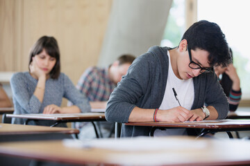 Focused male college student taking test at desk in classroom - obrazy, fototapety, plakaty