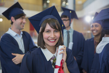 Portrait smiling female college graduate in cap gown holding diploma