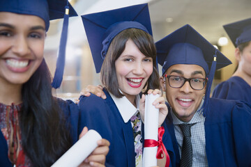Portrait enthusiastic college graduates in cap gown posing diploma