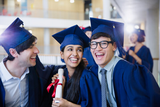 Happy college graduates in cap and gown celebrating with diploma
