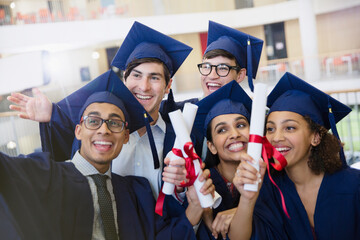 Happy college students in cap gown holding diplomas posing for selfie
