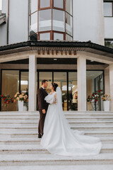 Obraz premium Groom and bride walking outdoors near a posh hotel. A long train of dress on the steps