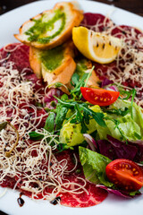 Appetizer of beef carpaccio with cherry tomatoes, cheese, salad, toasted bread and lemon.