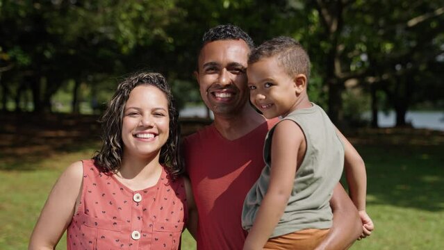 Latino family of mother, father and son standing at city park and smiling in front of the camera. Portrait shot. Outdoors
