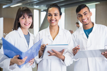 Portrait smiling college students in lab coats notebooks in science laboratory classroom