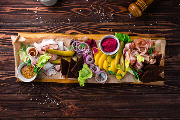 Banquet board with slices of bacon, boiled potatoes, red onion rings, pickles, garlic croutons,...