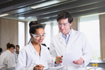 College students in lab coats discussing notes in science laboratory classroom