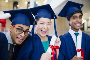 Portrait enthusiastic college graduates in cap gown holding diplomas