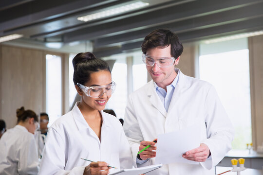 College students in lab coats discussing notes in science laboratory classroom