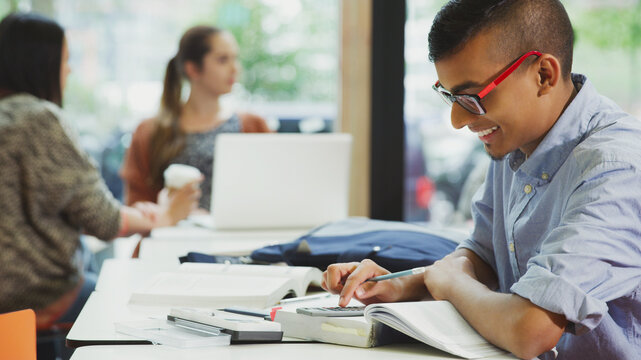 Male College Student Doing Math Homework With Textbook And Calculator