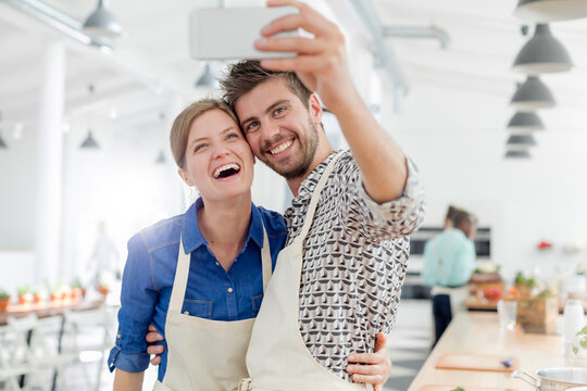 Enthusiastic couple taking selfie camera phone in cooking class kitchen