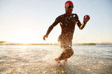 Male triathlete swimmer in wet suit running from ocean