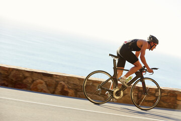 Male triathlete cyclist racing on ocean road - obrazy, fototapety, plakaty