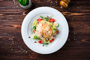 Italian Caesar salad with chicken, parmesan cheese, quail eggs, lettuce, tomatoes and croutons in a plate.