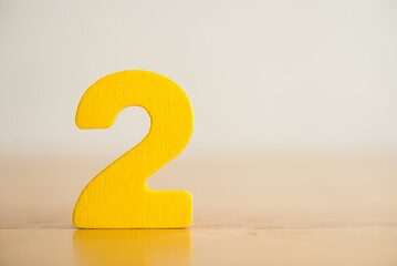 Wooden yellow number 2 (two) sign stand on wooden table white background with copy space. Number...