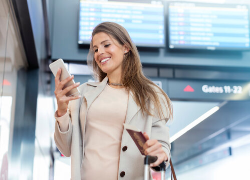 Businesswoman With Passport Using Cell Phone In Airport