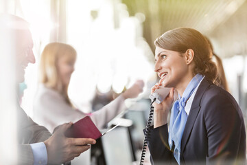 Customer service representative talking on telephone helping businessman at airport check-in counter