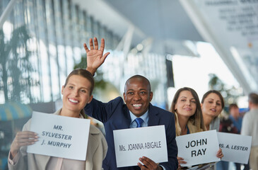 Chauffeurs with welcome signs smiling and waving in a row at airport