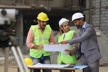 Indian construction workers. Construction engineers working on a builder construction site. Wearing white and yellow helmet analyzing blueprint of property. Reporting, maintaining the work in progress